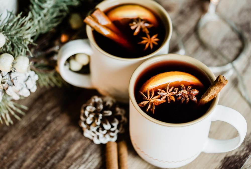 Gluehwein in weissen Bechern mit Gewuerzen, Zimt und Orange