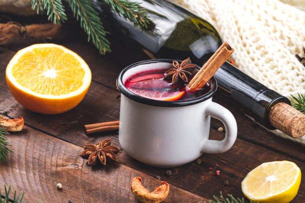 Gluehwein neben Rotweinflasche mit Gewuerzen und Zitrusfruechten